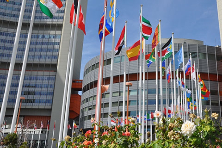 An exterior shot of the Vienna International Center on a sunny day with flags in foreground.
